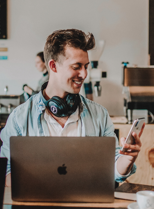 Photo of a developer on laptop, looking at phone, with headphones on